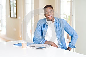 African american student man studying using notebooks and wearing headphones with a happy and cool smile on face