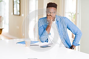 African american student man studying using notebooks and wearing headphones looking stressed and nervous with hands on mouth