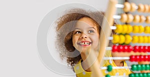 An african american student in a yellow dress laughs brightly behind a colored abacus in an elementary school