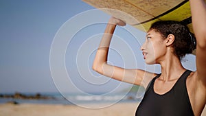 African american surfer standing with surf board on her head on ocean beach. Black woman looking at sea waves on lineup