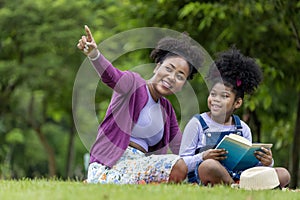 African American teacher is teaching her young student to read while having a summer outdoor class in the public park for