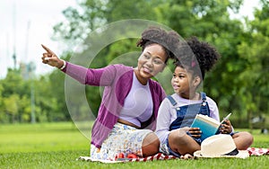 African American teacher is teaching her young student to read while having a summer outdoor class in the public park for