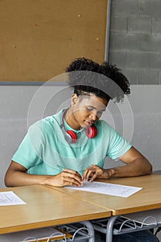 African american teen boy high school student sitting behind desk in classroom doing homework. Vertical image