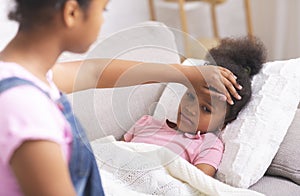 African american teen girl touching her sick little sister`s forehead