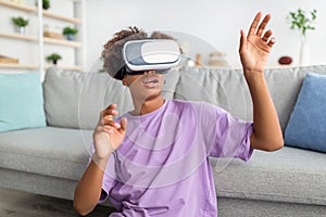 African American teen guy in virtual reality headset touching imaginary screen, exploring cyberspace at home