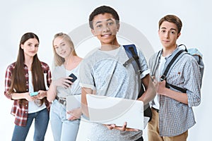 african american teenage boy holding laptop while friends standing near by