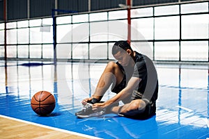 African American teenage boy tying his shoe laces on a basketball court