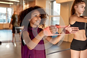 African american teenage girl working out using resistance band in gym together with other kids. Sport, healthy