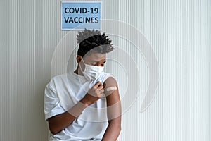 African American teenager looking adhesive bandages on his arm after received COVID-19 antiviral vaccine