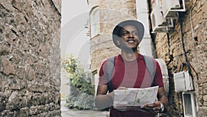 African american tourist man walking and watching paper city map to find directions to famous place
