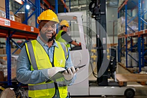 African American warehouse factory worker man hold cardboard and look at camera during working and stay in front other coworker