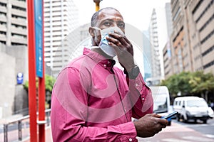 African American wearing covid19 coronavirus mask and using his phone in the street