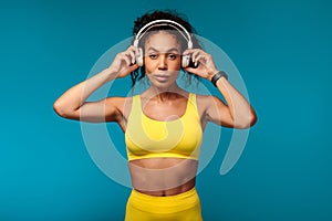 African American woman in activewear putting on earphones, blue backdrop