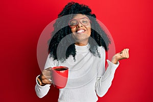 African american woman with afro hair holding coffee screaming proud, celebrating victory and success very excited with raised arm