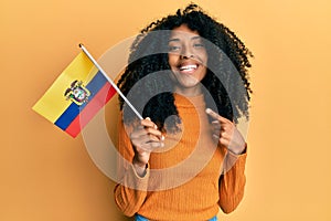 African american woman with afro hair holding ecuador flag smiling happy pointing with hand and finger