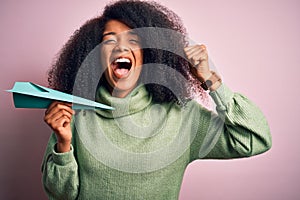 African american woman with afro hair holding paper plane as communication and success symbol screaming proud and celebrating