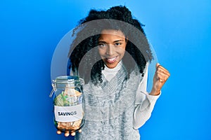 African american woman with afro hair holding savings jar with south african rands money screaming proud, celebrating victory and