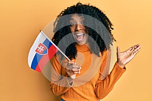 Afroameričanka s afro vlasmi drží vlajku slovenska oslavuje úspech so šťastným úsmevom a víťazným výrazom