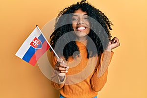 Afroameričanka s afro vlasy držící vlajku slovenska křičí hrdě, slaví vítězství a úspěch velmi nadšená