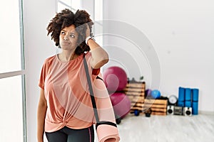 African american woman with afro hair holding yoga mat at pilates room confuse and wondering about question