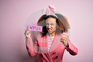 African american woman with afro hair wearing bunny ears holding paper with message annoyed and frustrated shouting with anger,