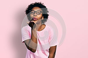 African american woman with afro hair wearing casual clothes and glasses looking at the camera blowing a kiss with hand on air