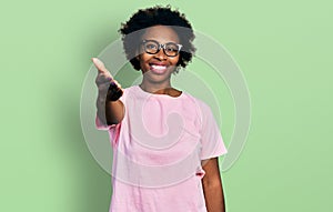 African american woman with afro hair wearing casual clothes and glasses smiling friendly offering handshake as greeting and