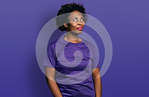 African american woman with afro hair wearing casual purple t shirt smiling looking to the side and staring away thinking