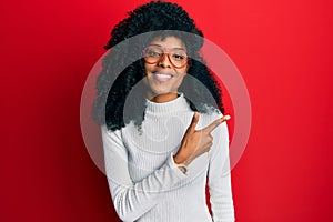 African american woman with afro hair wearing casual sweater and glasses smiling cheerful pointing with hand and finger up to the