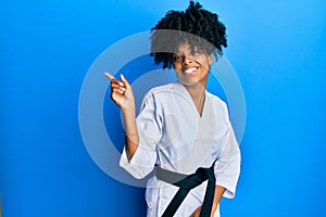 African american woman with afro hair wearing karate kimono and black belt with a big smile on face, pointing with hand and finger