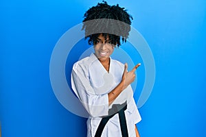 African american woman with afro hair wearing karate kimono and black belt cheerful with a smile of face pointing with hand and