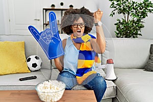 African american woman with afro hair wearing team scarf cheering game holding megaphone annoyed and frustrated shouting with