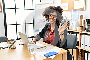 African american woman with afro hair working at the office wearing operator headset waiving saying hello happy and smiling,