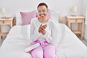 African american woman applying skin treatment sitting on bed at bedroom