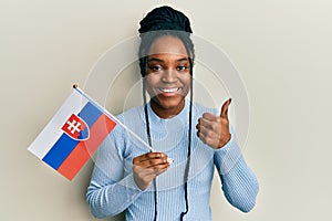Afroameričanka s vlasmi zapletenými do copu drží slovenskú vlajku s úsmevom šťastná a pozitívna, palec hore robí výborne a schvaľuje