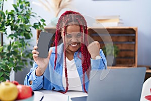 African american woman with braided hair holding smartphone showing blank screen screaming proud, celebrating victory and success