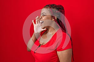 African american woman with braided hair standing over red background shouting and screaming loud to side with hand on mouth