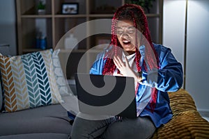 African american woman with braided hair using computer laptop at night doing stop gesture with hands palms, angry and frustration