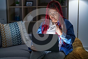 African american woman with braided hair using computer laptop at night showing middle finger, impolite and rude fuck off