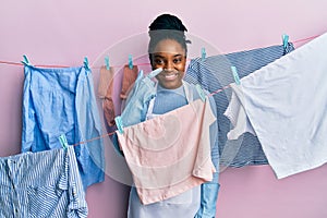 African american woman with braided hair washing clothes at clothesline pointing with hand finger to face and nose, smiling