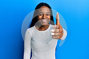 African american woman with braided hair wearing casual white sweater smiling friendly offering handshake as greeting and