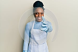 African american woman with braided hair wearing cleaner apron and gloves smiling friendly offering handshake as greeting and