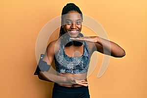 African american woman with braided hair wearing sportswear and arm band gesturing with hands showing big and large size sign,