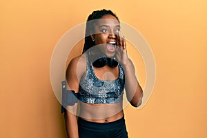 African american woman with braided hair wearing sportswear and arm band shouting and screaming loud to side with hand on mouth