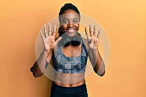 African american woman with braided hair wearing sportswear and arm band showing and pointing up with fingers number nine while