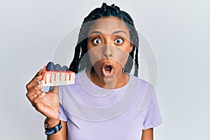 African american woman with braids holding a slice of cheesecake scared and amazed with open mouth for surprise, disbelief face
