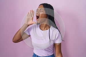 African american woman with braids standing over pink background shouting and screaming loud to side with hand on mouth