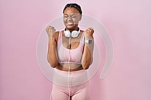 African american woman with braids wearing sportswear and headphones excited for success with arms raised and eyes closed
