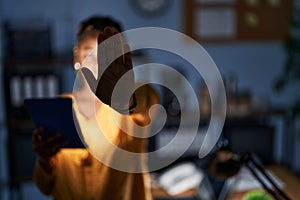 African american woman with braids working at the office at night with tablet doing stop sing with palm of the hand