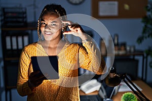 African american woman with braids working at the office at night with tablet smiling and confident gesturing with hand doing